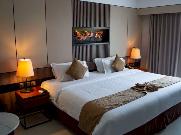 A neatly arranged hotel room with a large bed, decorative pillows, two bedside tables with lamps, and a window with curtains.