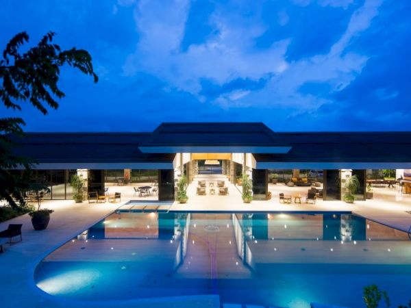 An illuminated resort building with an outdoor pool at twilight, featuring lounge chairs and a serene atmosphere under a blue, evening sky.