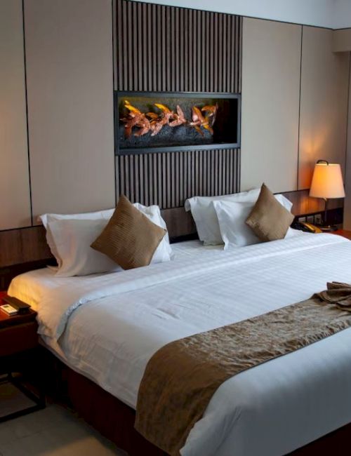 A well-decorated hotel room with a large bed, pillows, bedside tables with lamps, a wall-mounted artwork, and curtains covering a window.