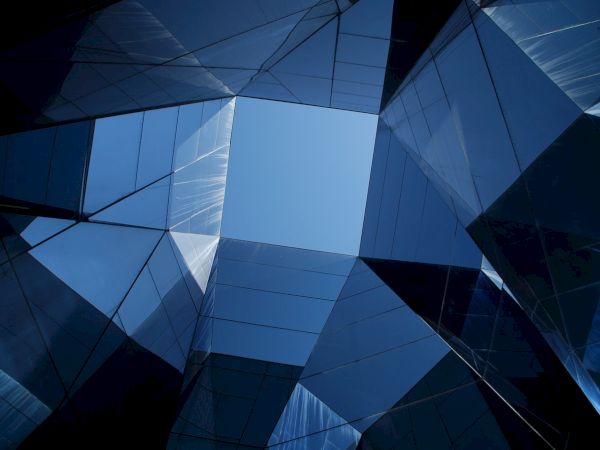 The image shows a series of mirror-like angular structures reflecting the sky, creating a geometric pattern with a blue sky visible in the center.