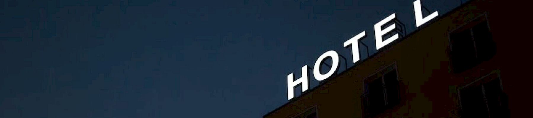 An illuminated "HOTEL" sign is displayed on a building at night, with the letter "L" slightly detached from the rest of the sign.