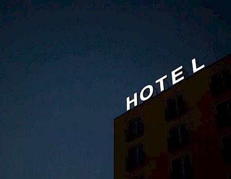 An illuminated "HOTEL" sign is displayed on a building at night, with the letter "L" slightly detached from the rest of the sign.