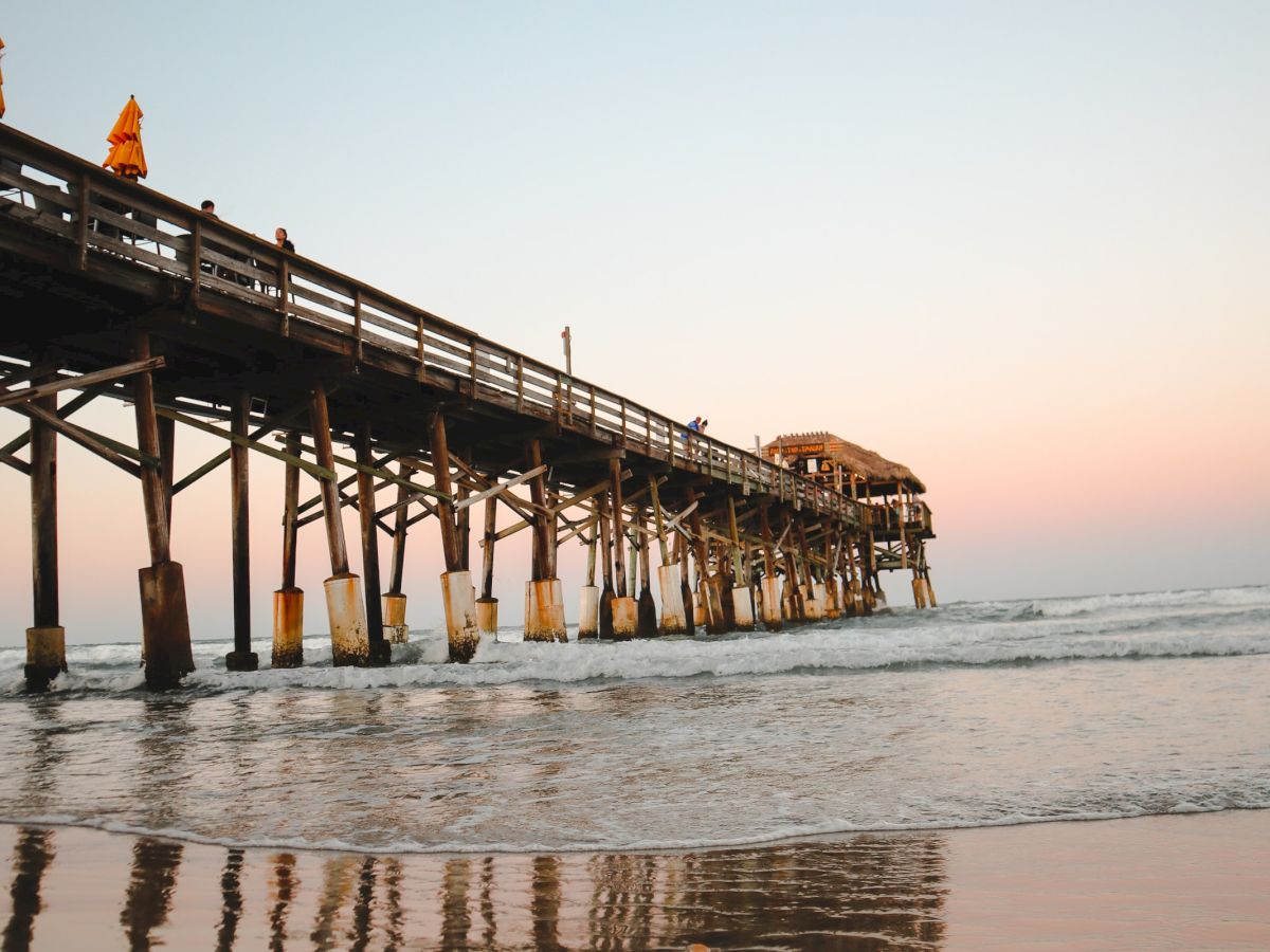 The image shows a pier extending over the ocean, with a clear sky and calm water reflecting the structure.