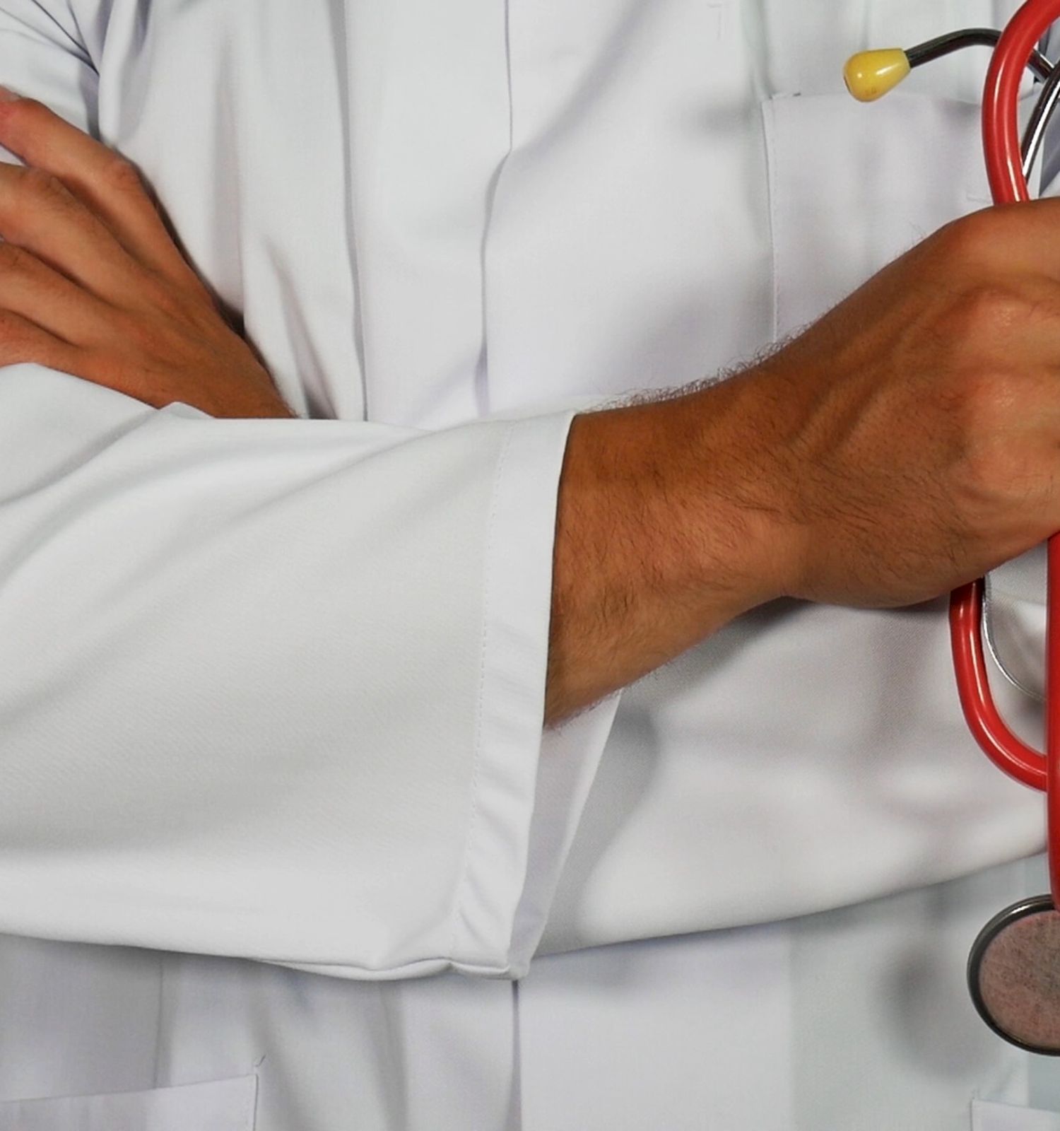 A person in a white medical coat is shown with arms crossed, holding a red stethoscope in the right hand.