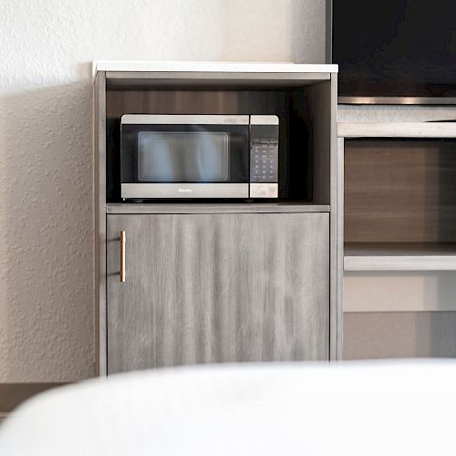 The image shows a microwave oven placed in a small wooden cabinet next to a television. The cabinet has a closed bottom section.