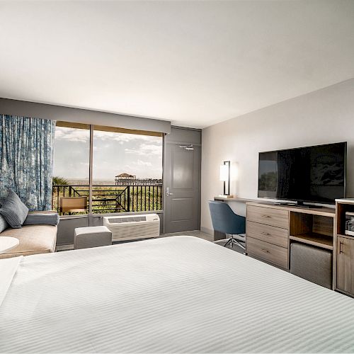 A modern hotel room features a large bed, a TV, a desk with a chair, a microwave, a mini-fridge, and a window with a scenic view ending the sentence.