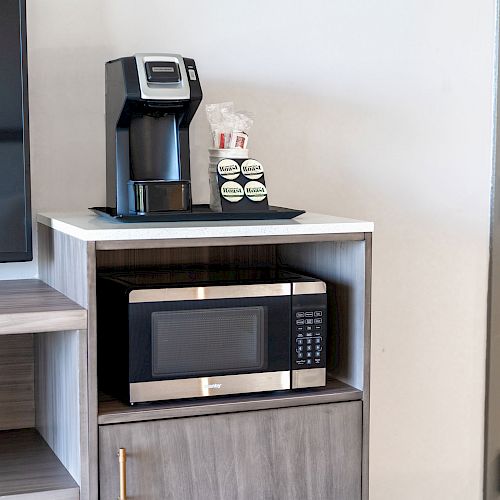 The image shows a coffee machine with coffee pods on top of a small cabinet and a microwave below it, adjacent to a door.