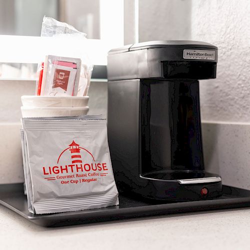 A coffee maker is on a black tray with coffee packets labeled 