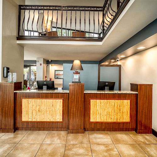 The image features a hotel reception area with two wooden front desks, a lamp in between, and a modern interior design.