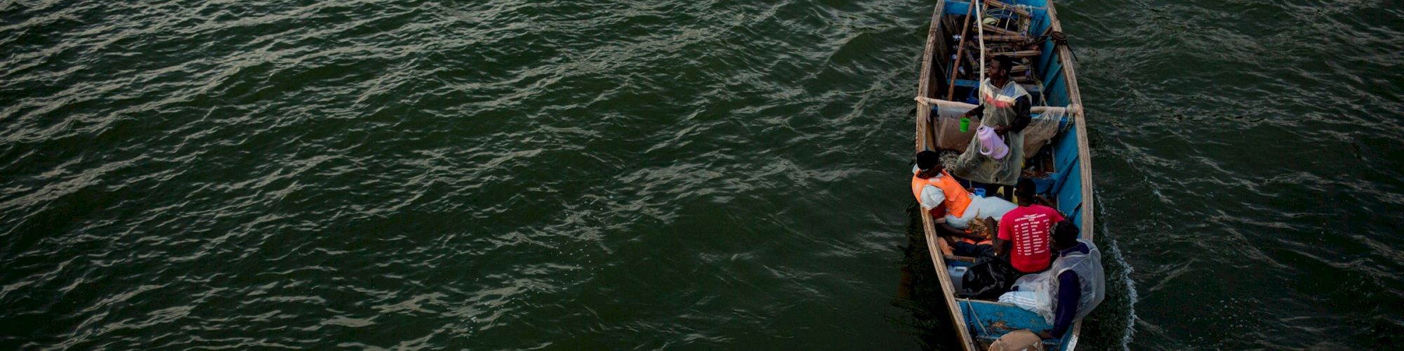 A small boat with four people in it is navigating through dark green water, creating a wake behind.