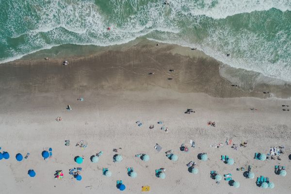 Aerial view of a beach with umbrellas and people along the shore; waves breaking on the sandy beach.