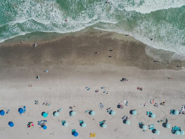 Aerial view of a beach with umbrellas and people along the shore; waves breaking on the sandy beach.