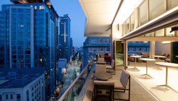 A modern balcony at dusk offering a cityscape view, with tables and chairs arranged neatly and high-rise buildings in the background.
