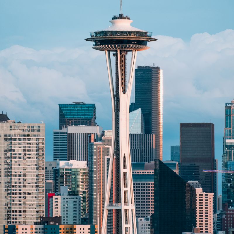 The image shows the Space Needle, a famous observation tower in Seattle, with the city skyline and various modern buildings in the background.