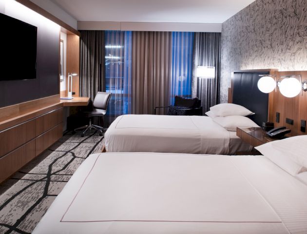 The image shows a modern hotel room with two neatly made beds, a flat-screen TV, a desk with a chair, and a stylish wall design ending the sentence.