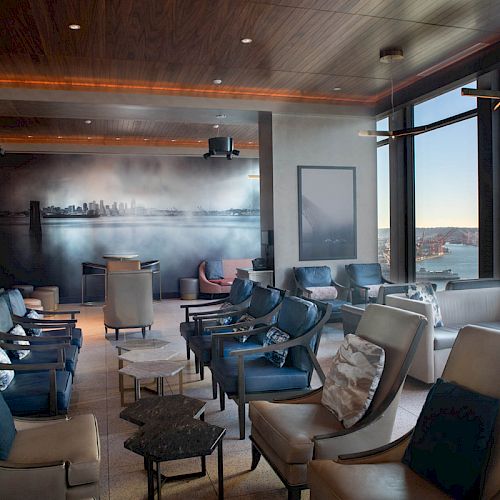 A modern lounge area with ample seating, large windows offering a scenic view of the water and a ferris wheel, and a mural of a city skyline.