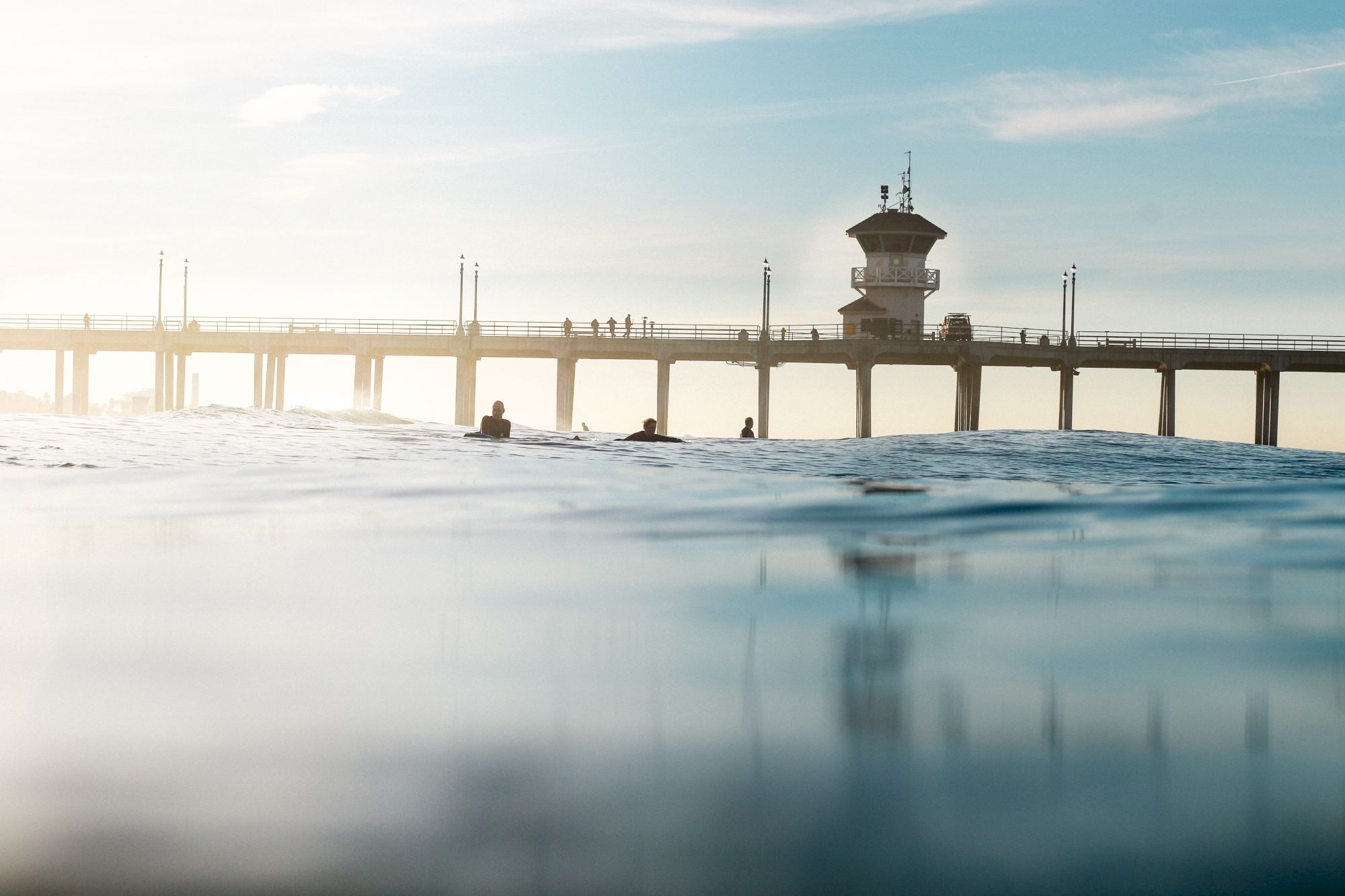 The image shows a serene view of a pier with several people and a lifeguard tower, viewed from the water's surface under a clear sky.
